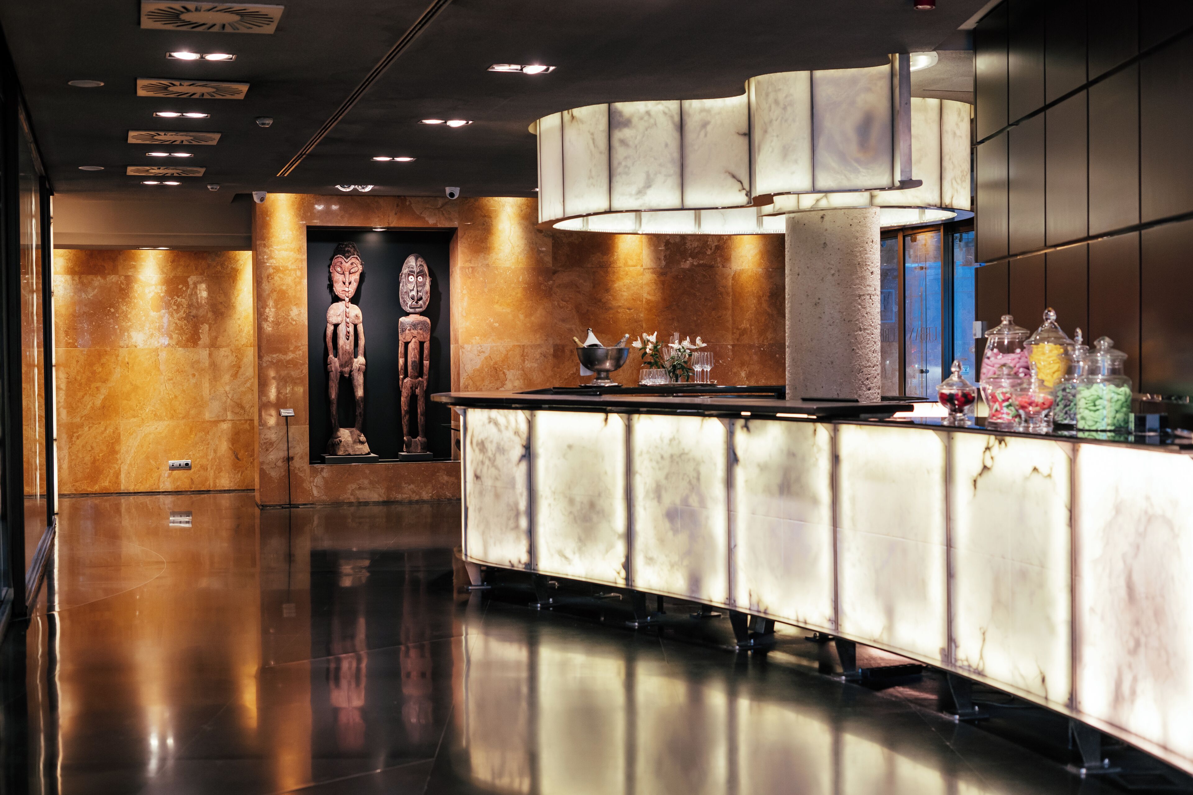 Un moderno vestíbulo de hotel con un mostrador de recepción de mármol pulido, una lámpara decorativa de gran tamaño y una escultura adosada a la pared.