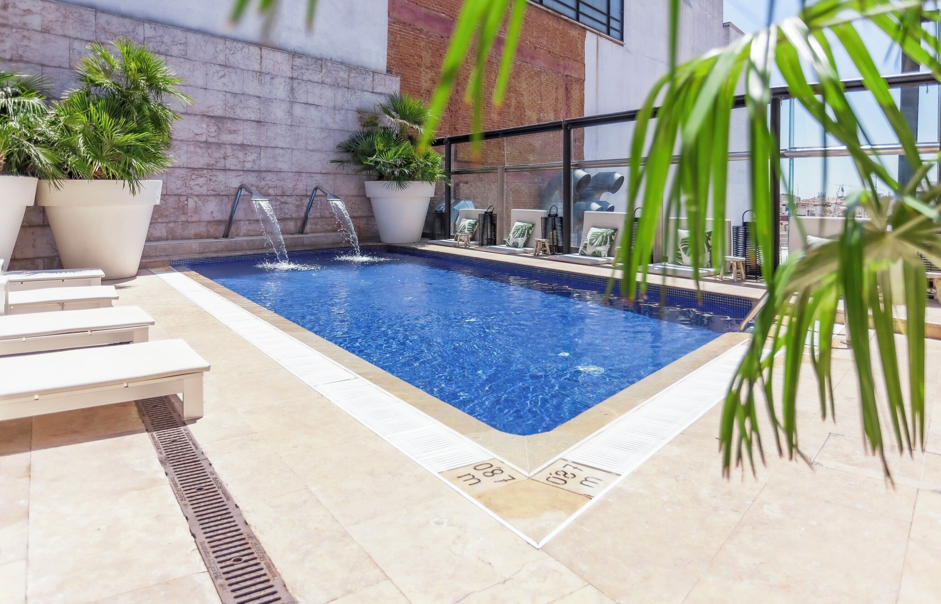 Ein Innenpool mit mehreren Wasserstrahlen, umgeben von Liegestühlen und Topfpflanzen.