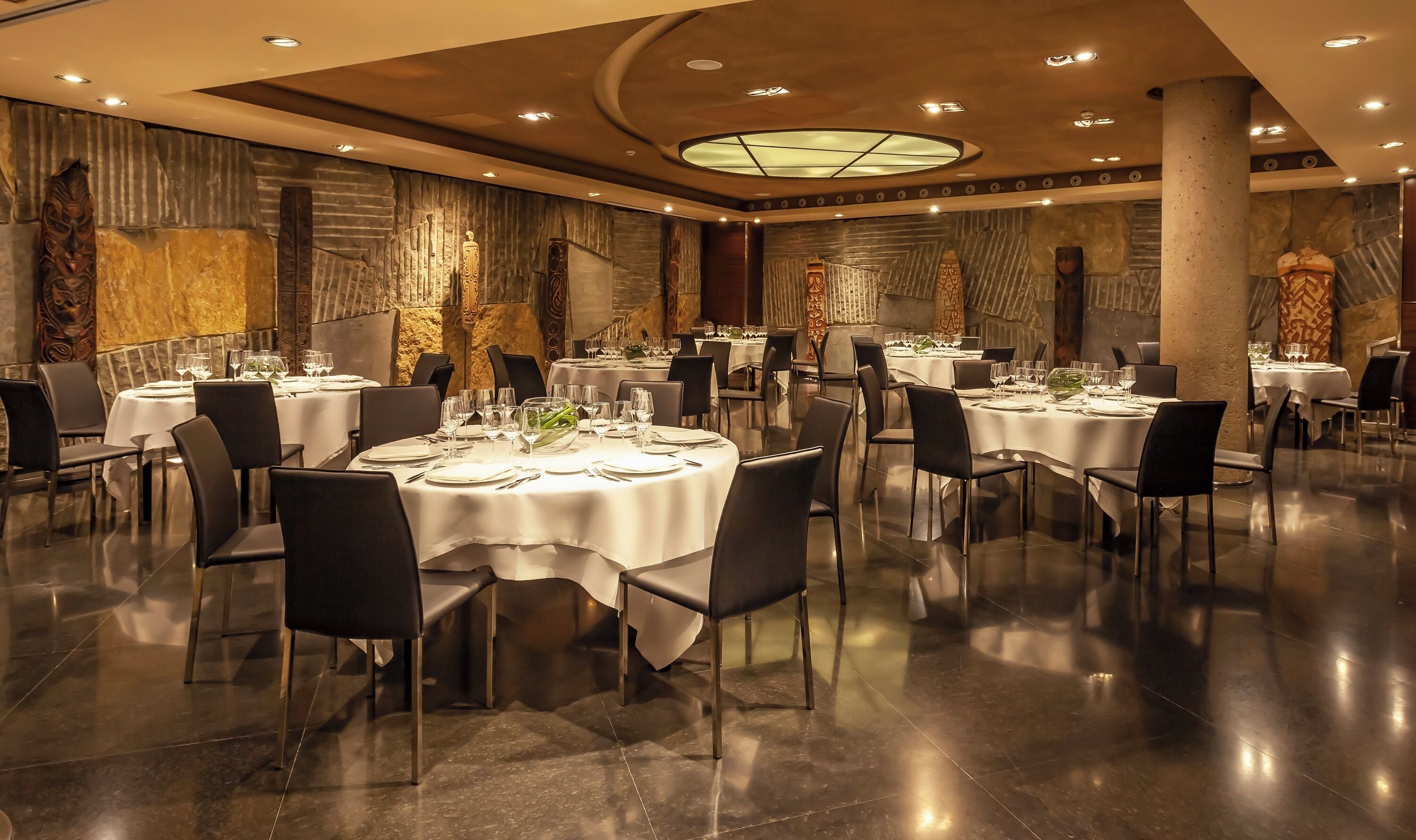 A spacious dining area with round tables, black chairs, and a modern ceiling design.