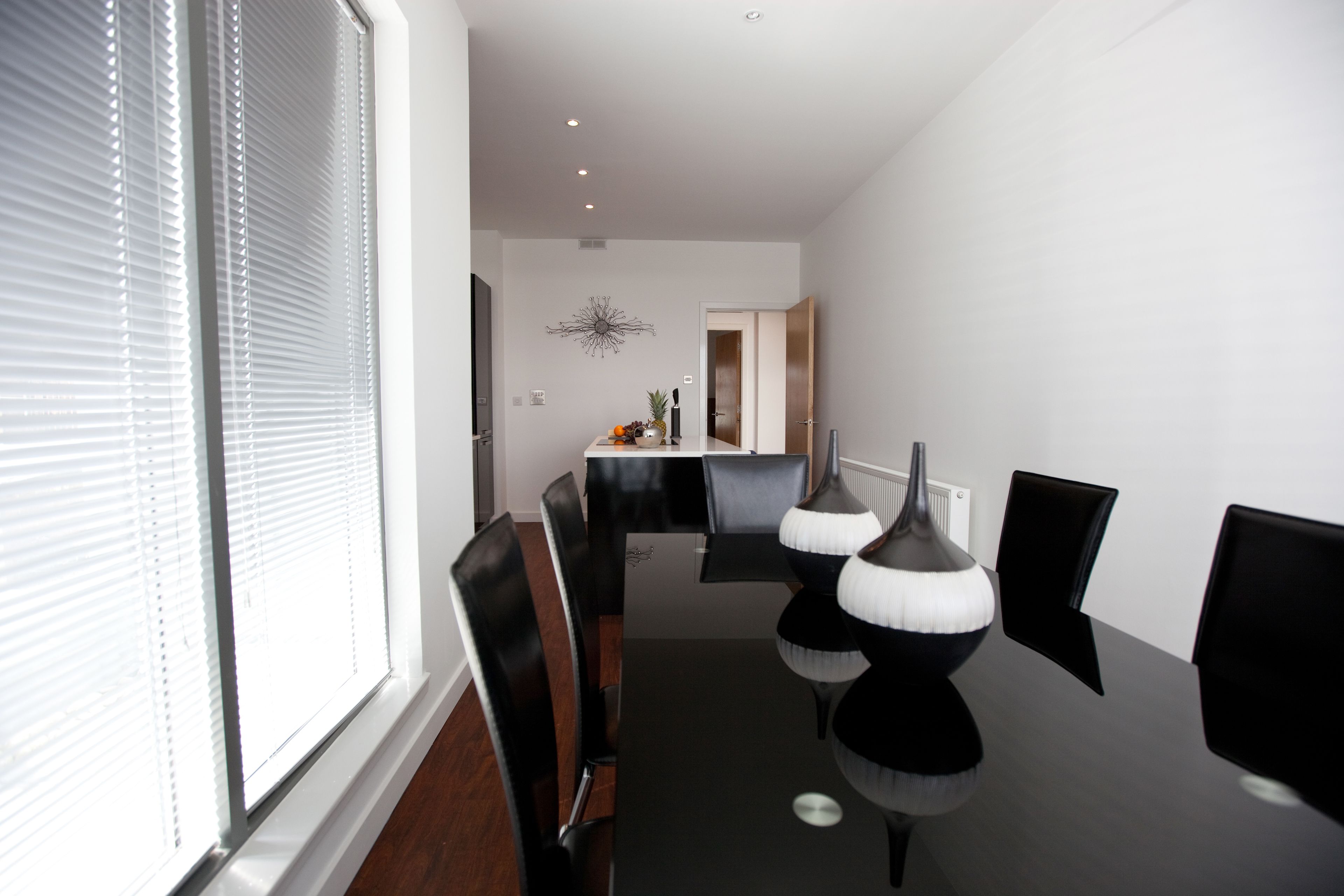 A modern dining area with a black table and chairs, a decorative wall piece, and a window with blinds.