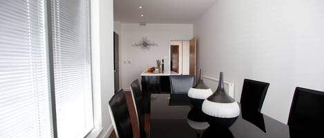 A modern dining area with a black table and chairs, a decorative wall piece, and a window with blinds.
