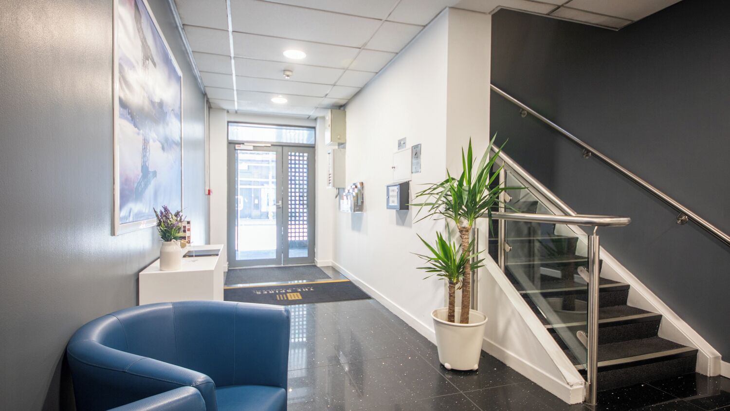 Um interior moderno com uma cadeira azul, uma escada e um vaso de planta.