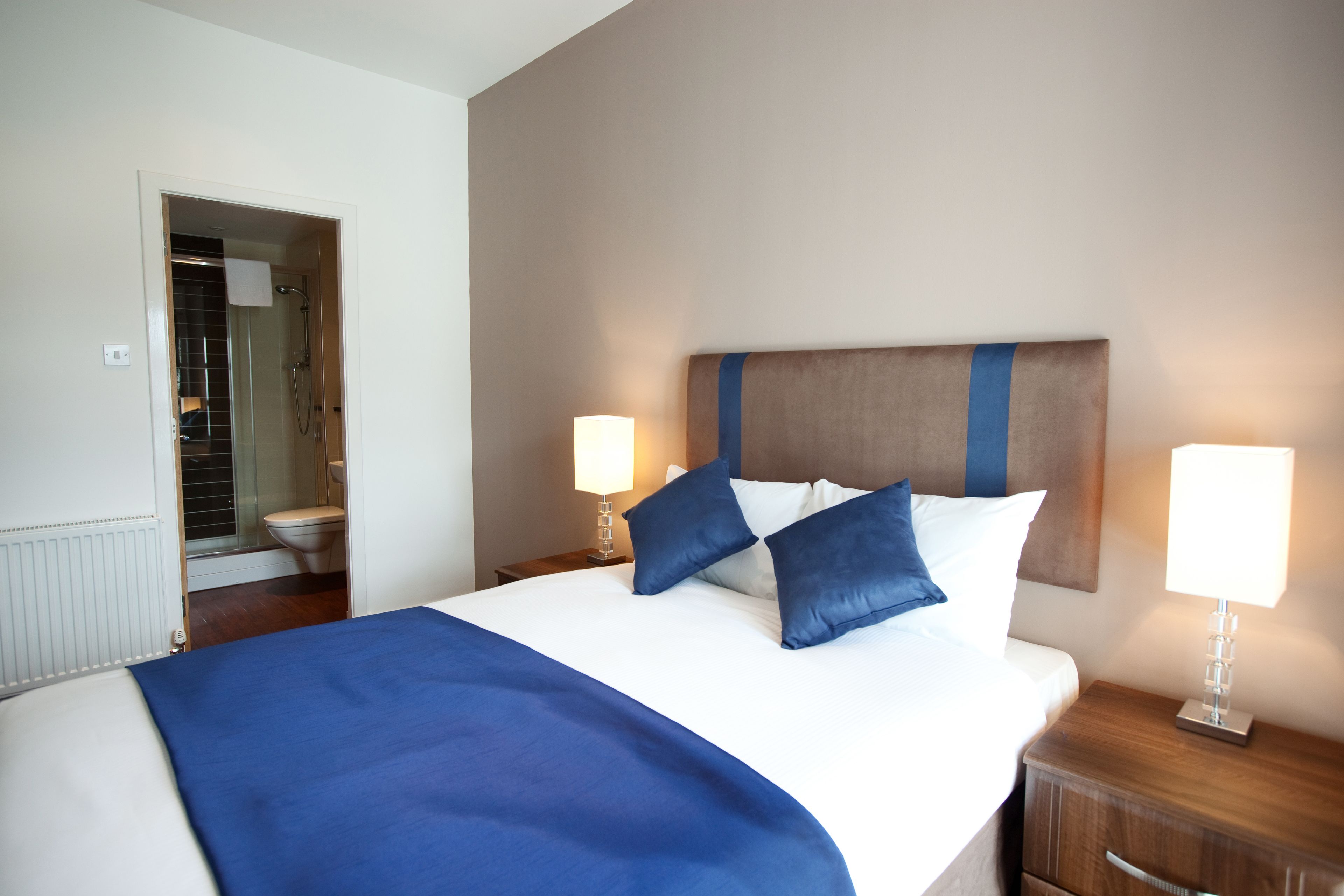 A hotel room with a large bed, two bedside lamps, a wooden headboard, and a bathroom visible through an open door.
