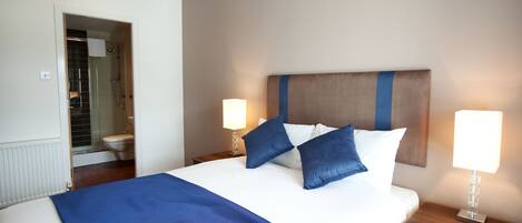 A hotel room with a large bed, two bedside lamps, a wooden headboard, and a bathroom visible through an open door.