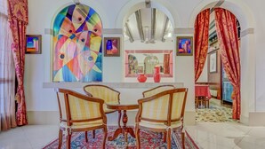 A dining area with a round table and four chairs, a colorful abstract painting, and a mirror above the table. - Hotel Hesperia (Venice)