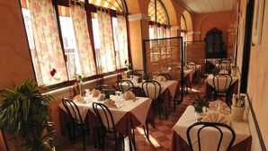 Un comedor con piso a cuadros, mesas dispuestas con manteles blancos y sillas.