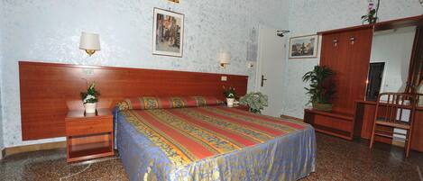 Una camera da letto con una testiera in legno, un letto con copriletto colorato, due comodini con lampade, uno specchio e una porta che dà su un'altra stanza.