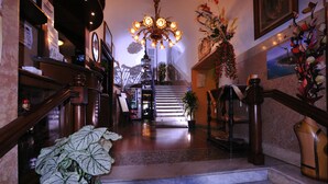 Una imponente escalera con un candelabro, peldaños de mármol y una planta en maceta.