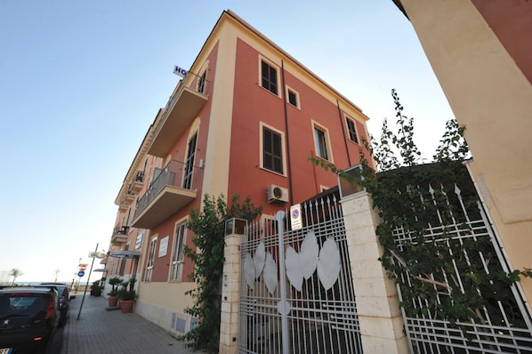 A multi-story building with balconies, a gated entrance, and potted plants.