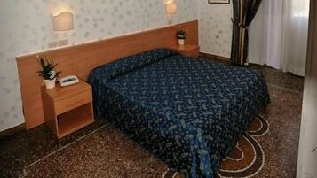 A bedroom with a wooden headboard, a single bed with a patterned bedspread, a ceiling fan, two bedside lamps, a small bedside table with a plant, and a wall-mounted TV.