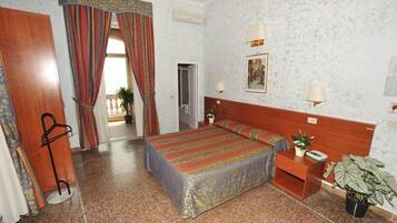Une chambre d’hôtel comprenant un lit, des tables de chevet, une petite table, une plante en pot et une porte donnant sur une autre pièce.