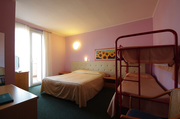 Et hotelværelse med køjeseng, en enkeltseng, et skrivebord med en bærbar computer, en stol, et vindue med gardiner, et billede af solsikker og en vægmonteret lampe.