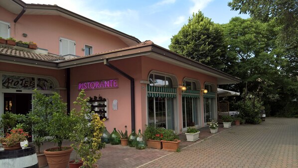 A pink building with a 'Ristorante' sign, potted plants, and a paved walkway. - Hotel Ristorante alla Campagna (San Giovanni Lupatoto)