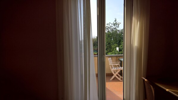 A view through a sliding glass door to an outdoor balcony with a white chair and a hanging planter. - Hotel Ristorante alla Campagna (San Giovanni Lupatoto)