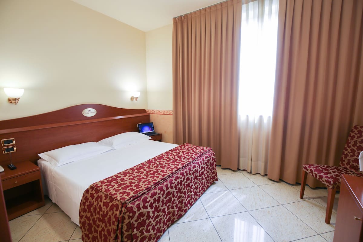 A hotel room with a bed, a desk, a chair, and a nightstand.