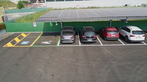 A parking area with four cars, a disabled parking space, and a solar panel roof.