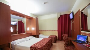 A hotel room with two beds, a desk with a laptop, a chair, and a TV on the wall.