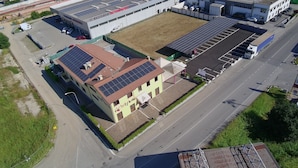 An industrial building with solar panels on the roof, a parking lot, and a road adjacent to it.