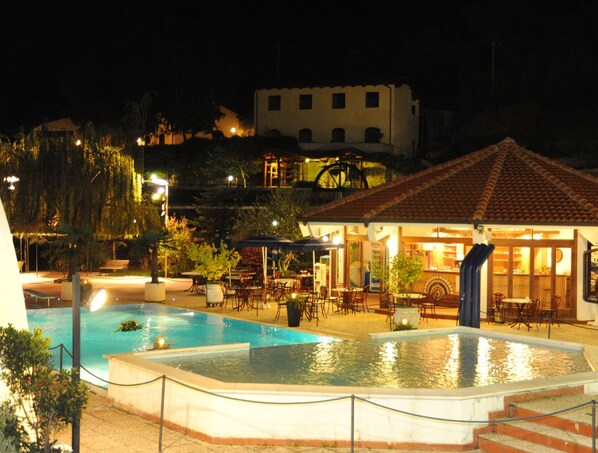 A nighttime view of a hotel with a pool area, outdoor seating, and a building with a tiled roof. - Hotel Ristorante Lago Bin (Rocchetta Nervina)