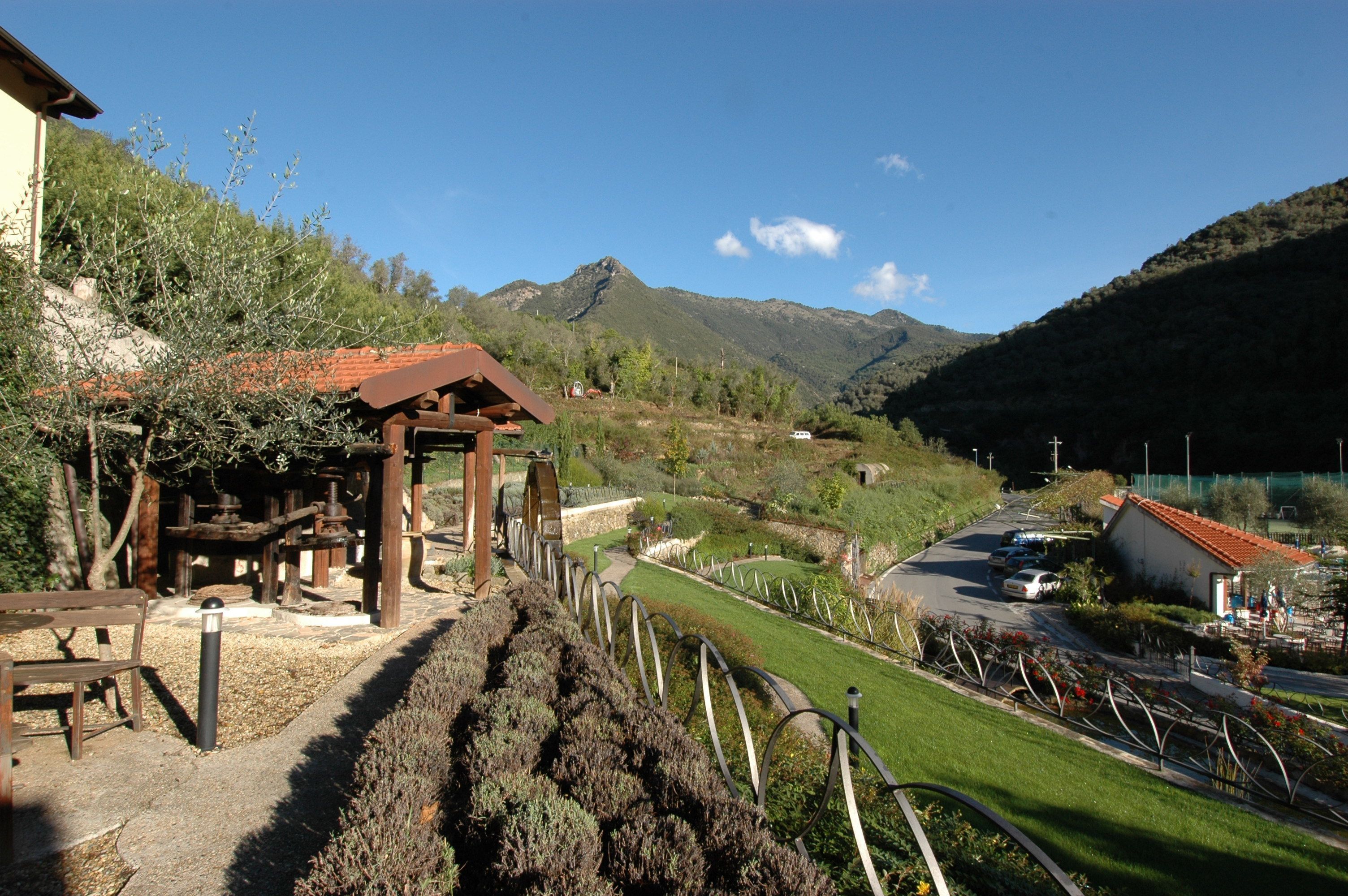 Un paysage rural avec un kiosque en bois, un chemin pavé et une route bordée de voitures garées.