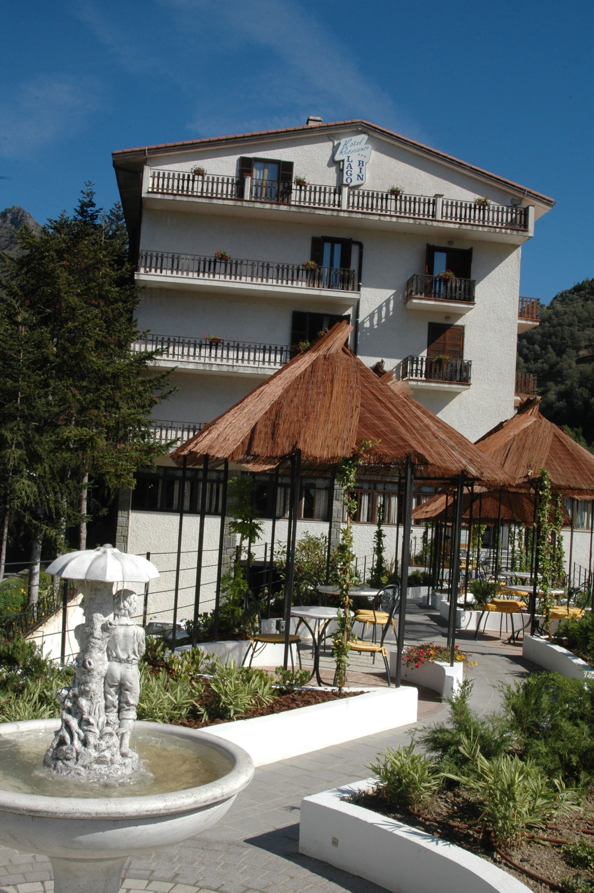 Ein Hotel mit weißer Fassade, mehreren Balkonen und Sitzbereichen im Freien mit Reetdach.