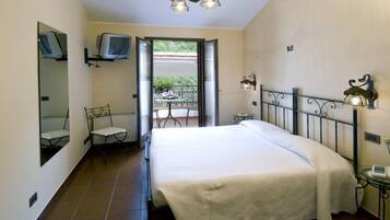 Un dormitorio con cama, una silla, televisor y balcón con vistas a la vegetación.