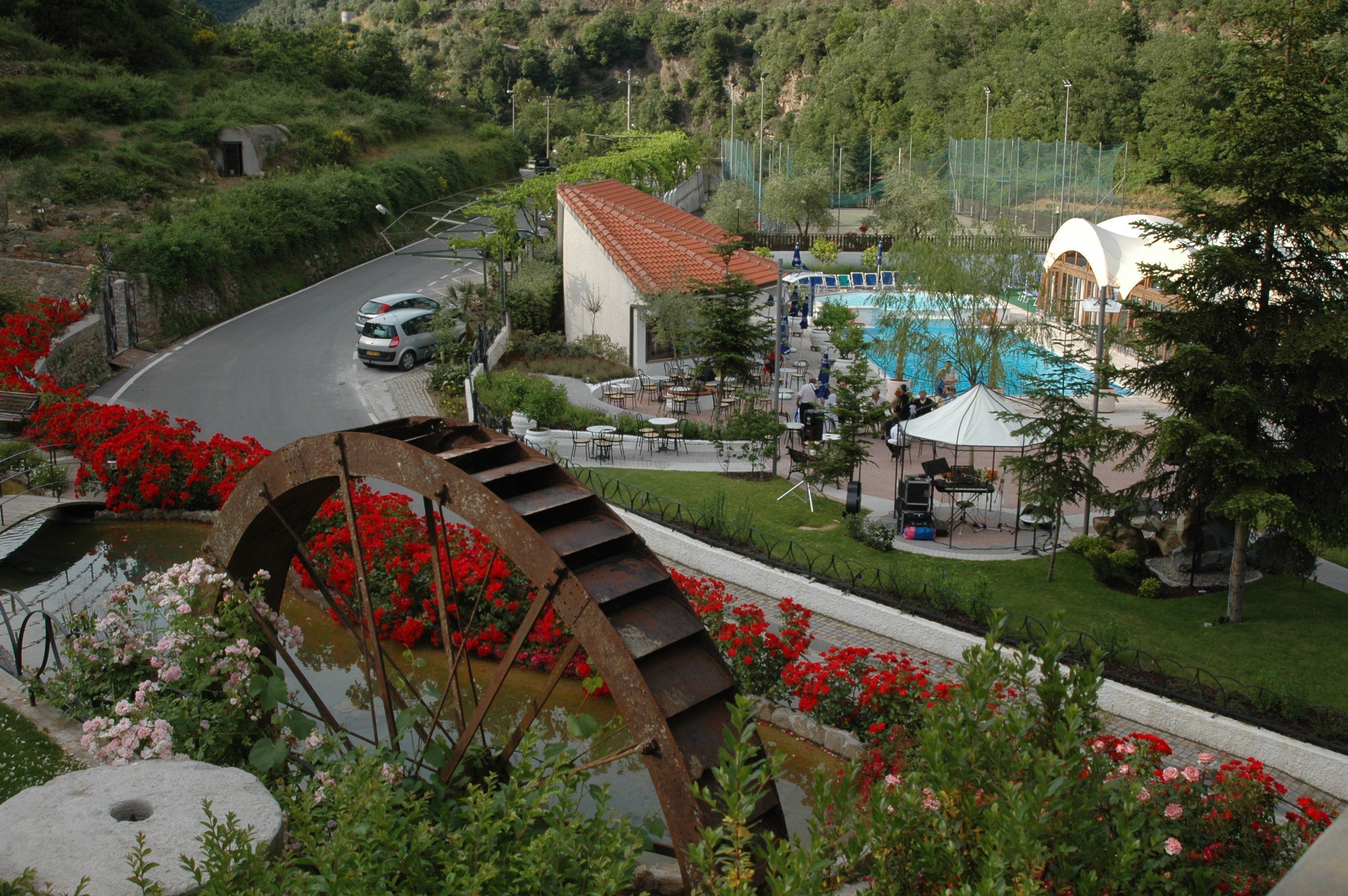 A hotel with a swimming pool, outdoor seating, and a large water wheel.