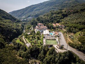 A large, white building with a swimming pool and tennis court, surrounded by lush greenery and hills. - Hotel Ristorante Lago Bin (Rocchetta Nervina)