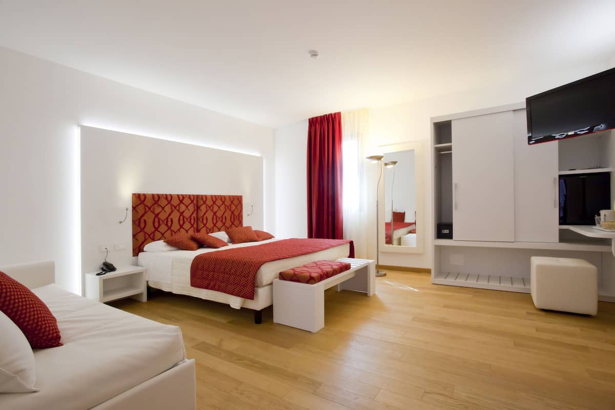 A modern hotel room with a large bed, a desk, a wardrobe, and a television.