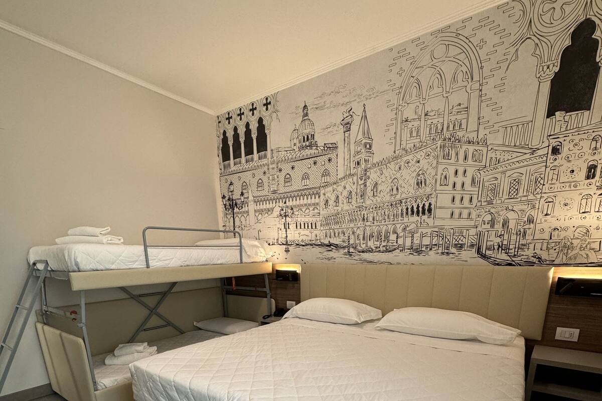 A room with a large bed, a bunk bed, and a mural of a cityscape on the wall.