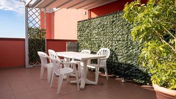 Un patio con una mesa y sillas blancas, una pared verde y frondosa, y una planta en maceta.