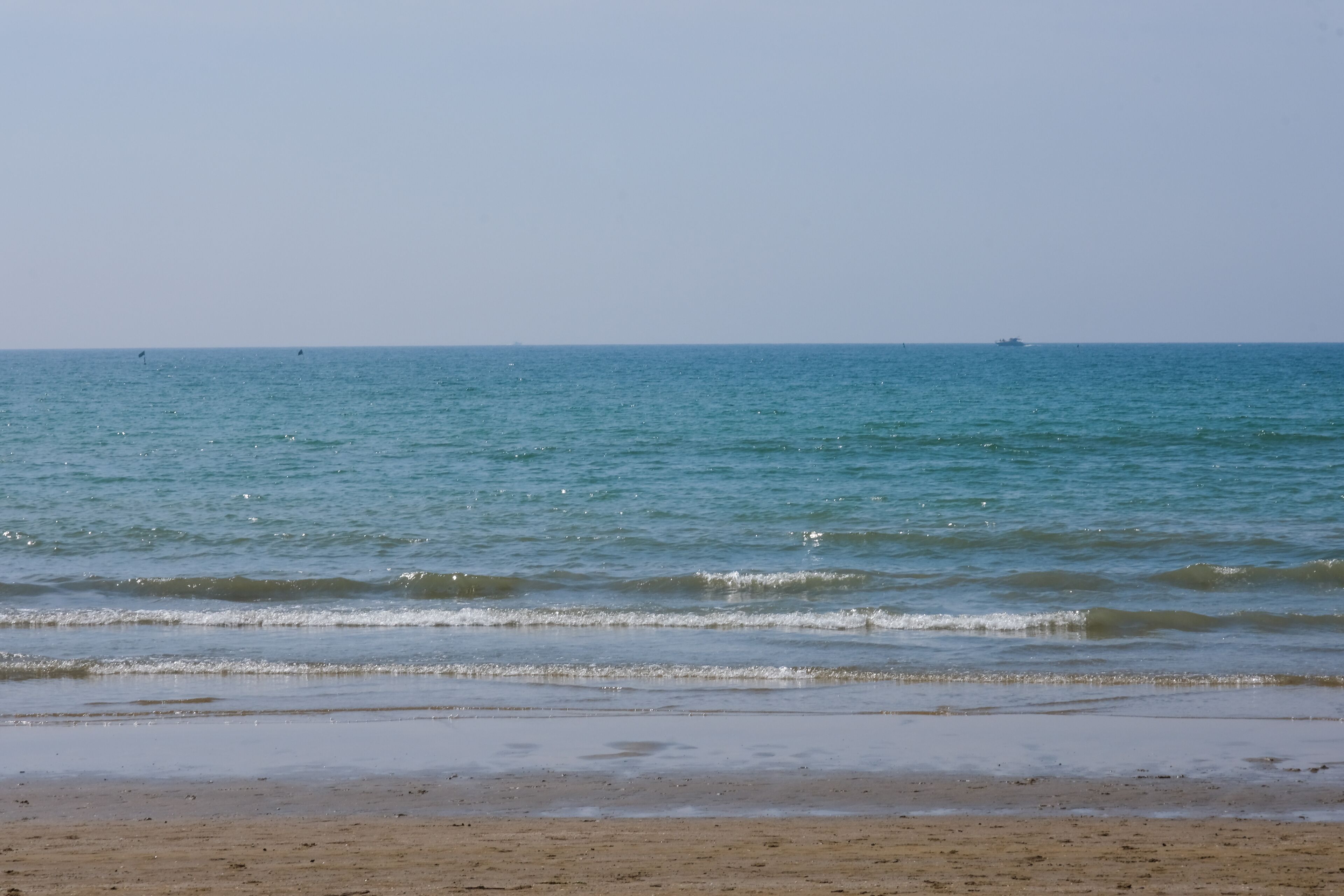 Ein Strand mit ruhigem Wasser und einem Schiffen im Hintergrund.