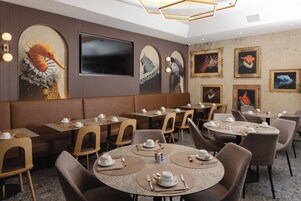 Restaurante com mesas redondas, cadeiras marrons e teto alto com luminária geométrica.