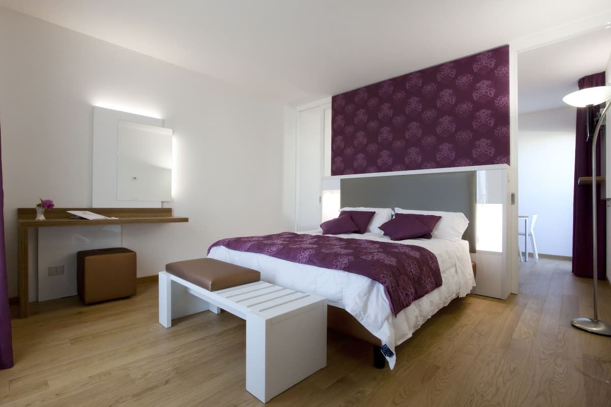 A modern bedroom with a bed, bedside table, bench, and a desk with a chair.