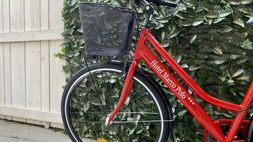 Uma bicicleta vermelha com cesto e estrutura vermelha, estacionada junto a uma cerca de madeira e folhagem verde.
