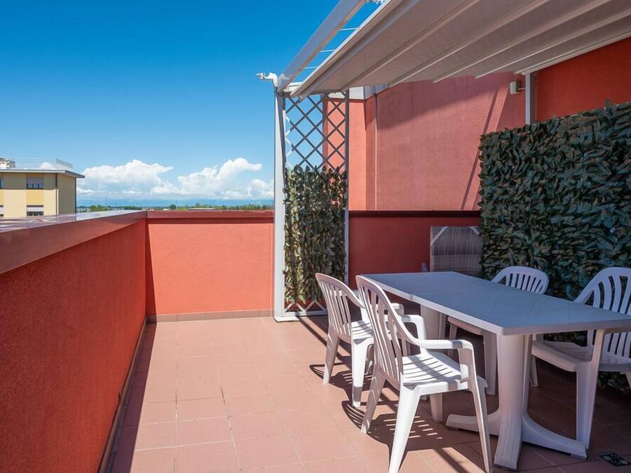 Une terrasse sur le toit avec une table et des chaises blanches, une haie verte et un ciel bleu dégagé.
