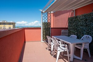 Um terraço no telhado com mesa e cadeiras brancas, um viveiro verde e um céu azul límpido.