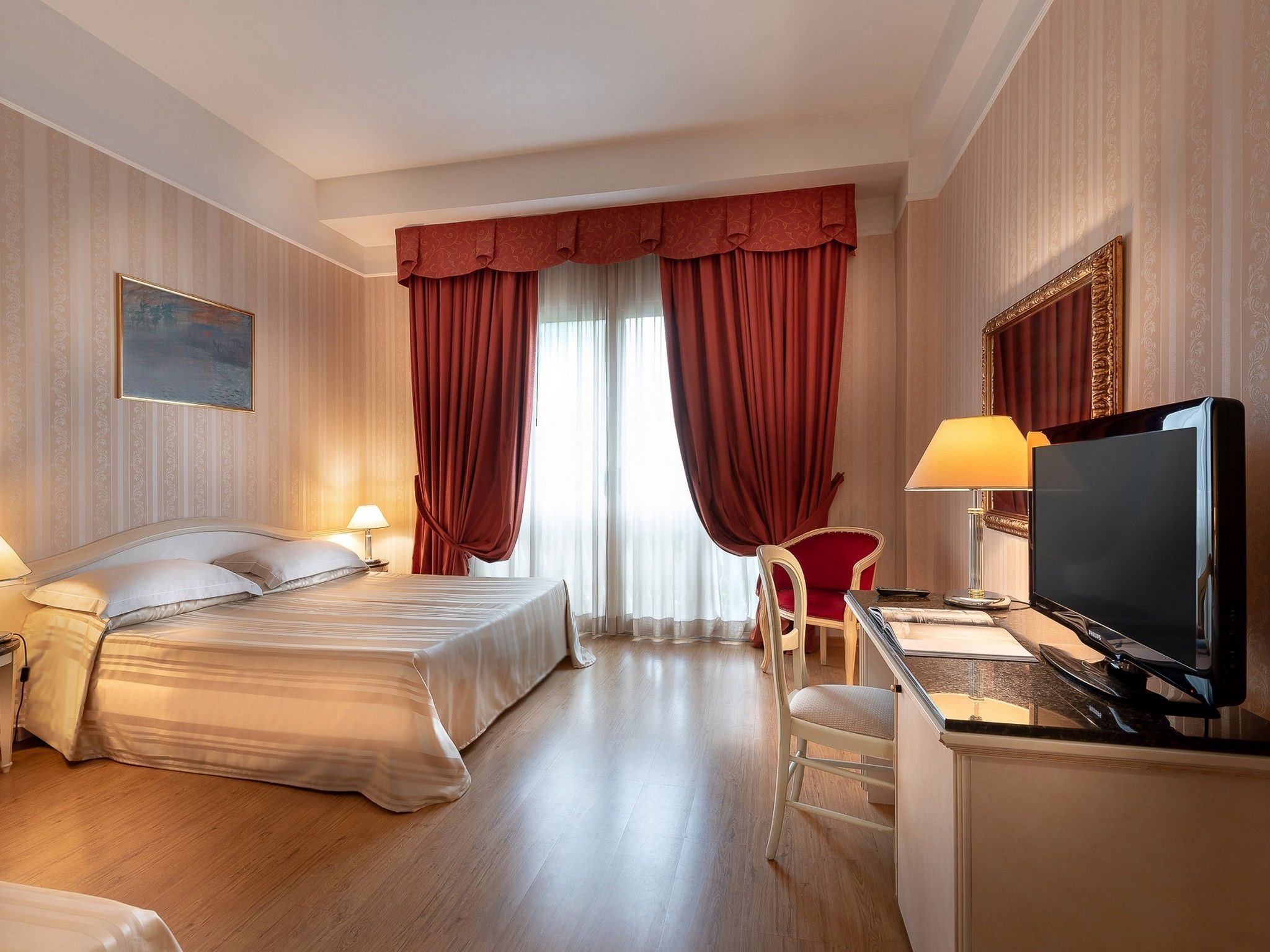 Une chambre d’hôtel avec un lit, un bureau avec un ordinateur, une télévision et une chaise.