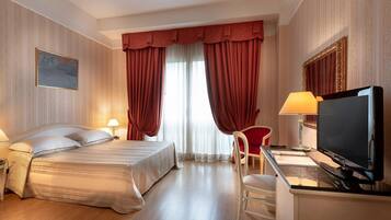Une chambre d’hôtel avec un lit, un bureau avec un ordinateur, une télévision et une chaise.