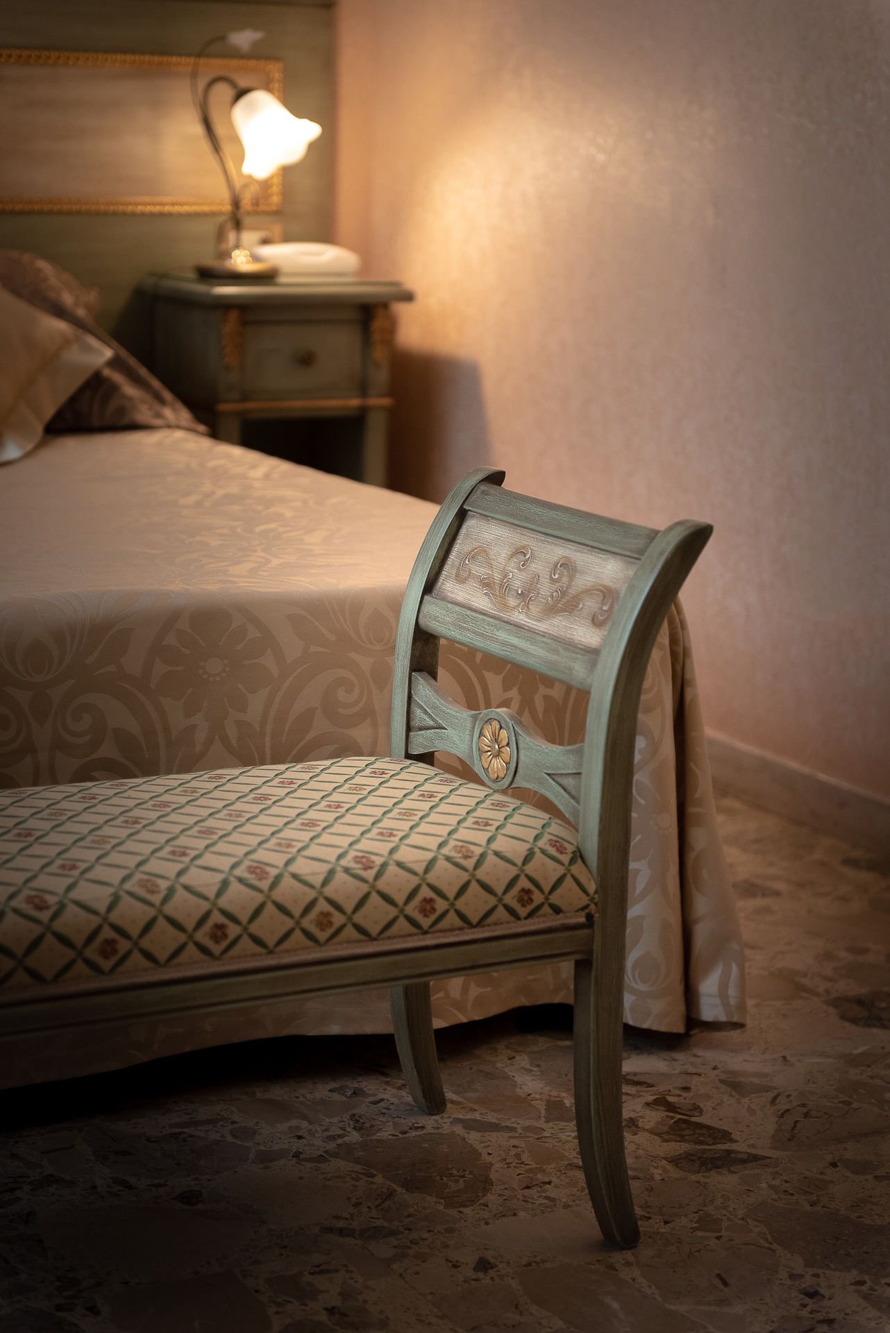 Un lit avec une couvre-lit à motifs, une lampe de chevet et une chaise agrémentée d’un coussin à fleurs.