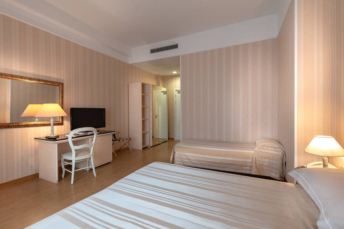 Ein Hotelzimmer mit zwei Betten, einem Schreibtisch mit Stuhl, einem Fernseher und einem Spiegel.