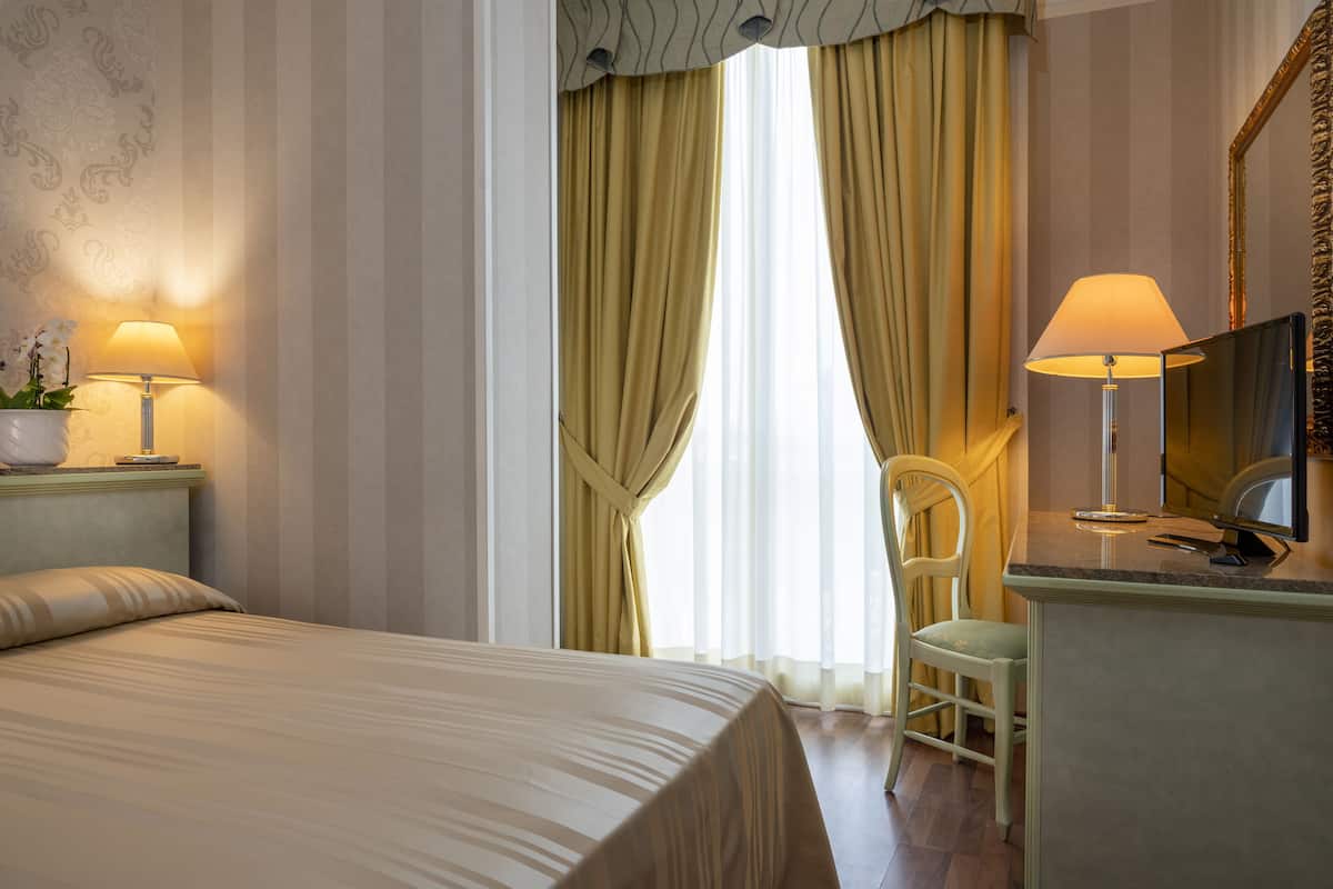 Ein Hotelzimmer mit Bett, Schreibtisch mit Lampe, Stuhl und Fernseher.
