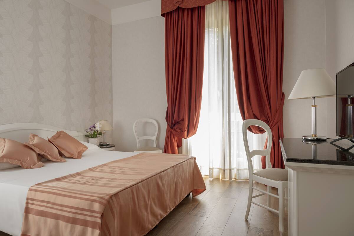 Ein ordentlich eingerichtetes Hotelzimmer mit einem Bett, einem Schreibtisch und einem Stuhl.