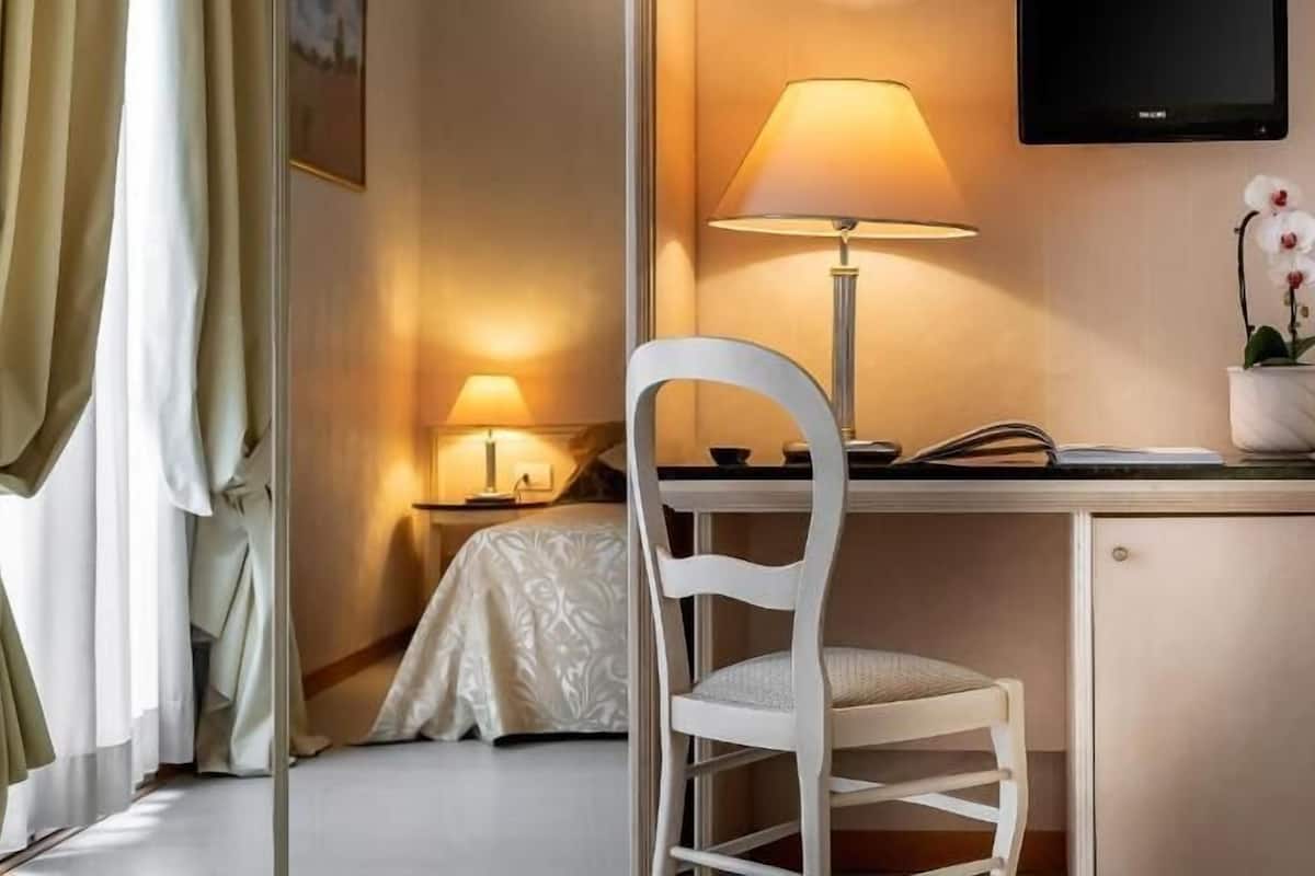 Ein Hotelzimmer mit Schreibtisch, Stuhl, Nachttisch, Lampe, Fernseher und einer Topfpflanze.