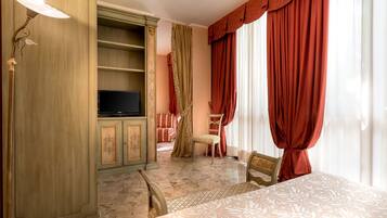 A hotel room with a television on a wooden cabinet, a bed with a patterned bedspread, a chair, and red curtains.