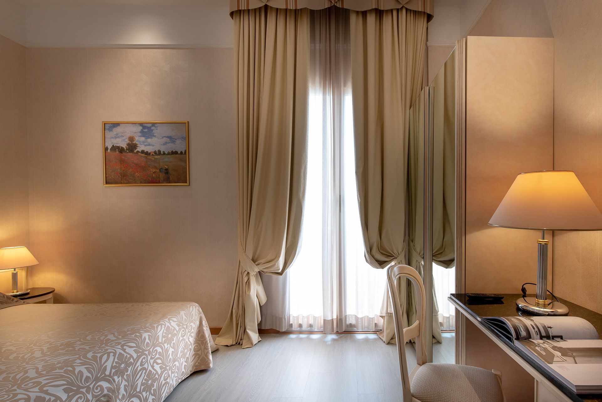 Une chambre d’hôtel avec un lit, un bureau doté d’une lampe, une chaise et un tableau au mur.