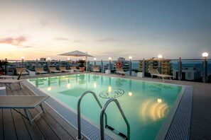 Una piscina en la azotea con sillones de descanso y un flotador salvavidas, rodeada de vistas urbanas.