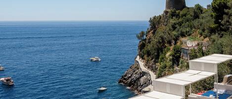 A seaside hotel with outdoor seating overlooking the sea, a rocky cliff, and a tower.