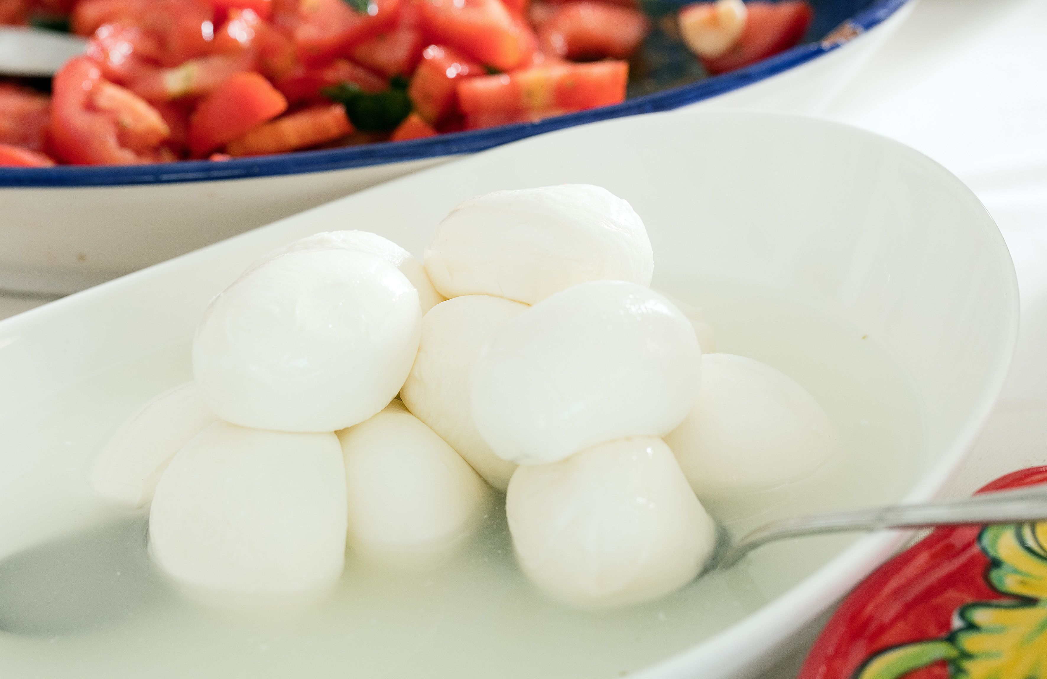 Un plato blanco con esferas blancas de comida, una cuchara, y un tazón con verduras rojas y verdes al fondo.