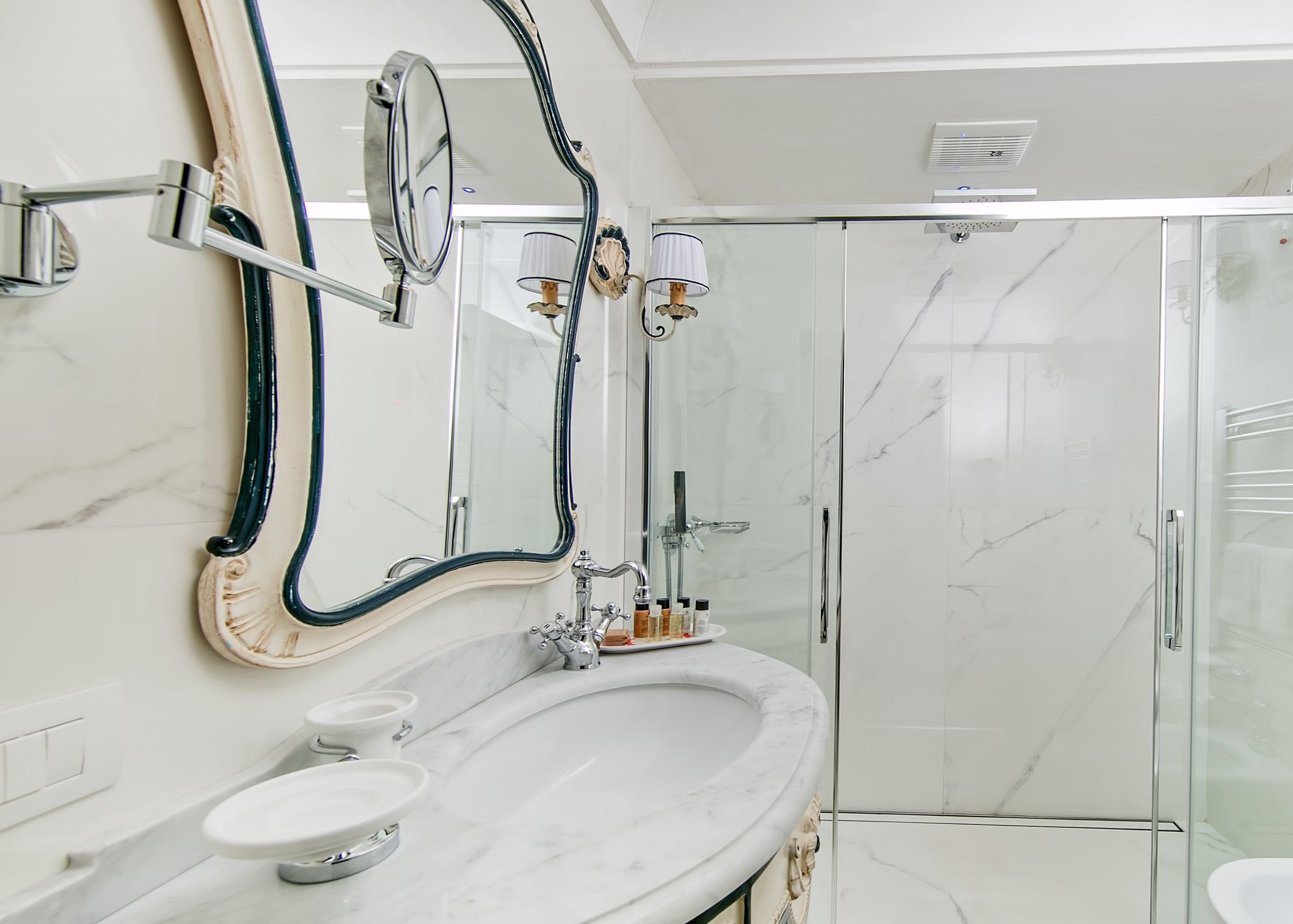 Un baño con lavamanos de mármol, dos espejos, cabina de ducha con vidrio y un perchero para toallas.